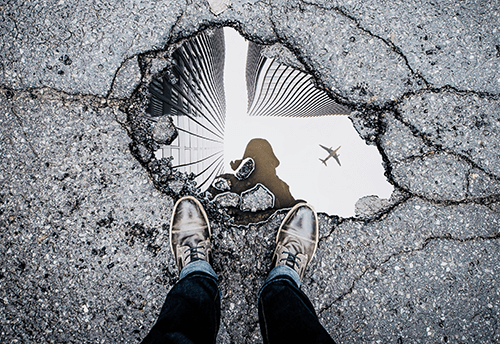 person standing over water filled puddle with plane reflected